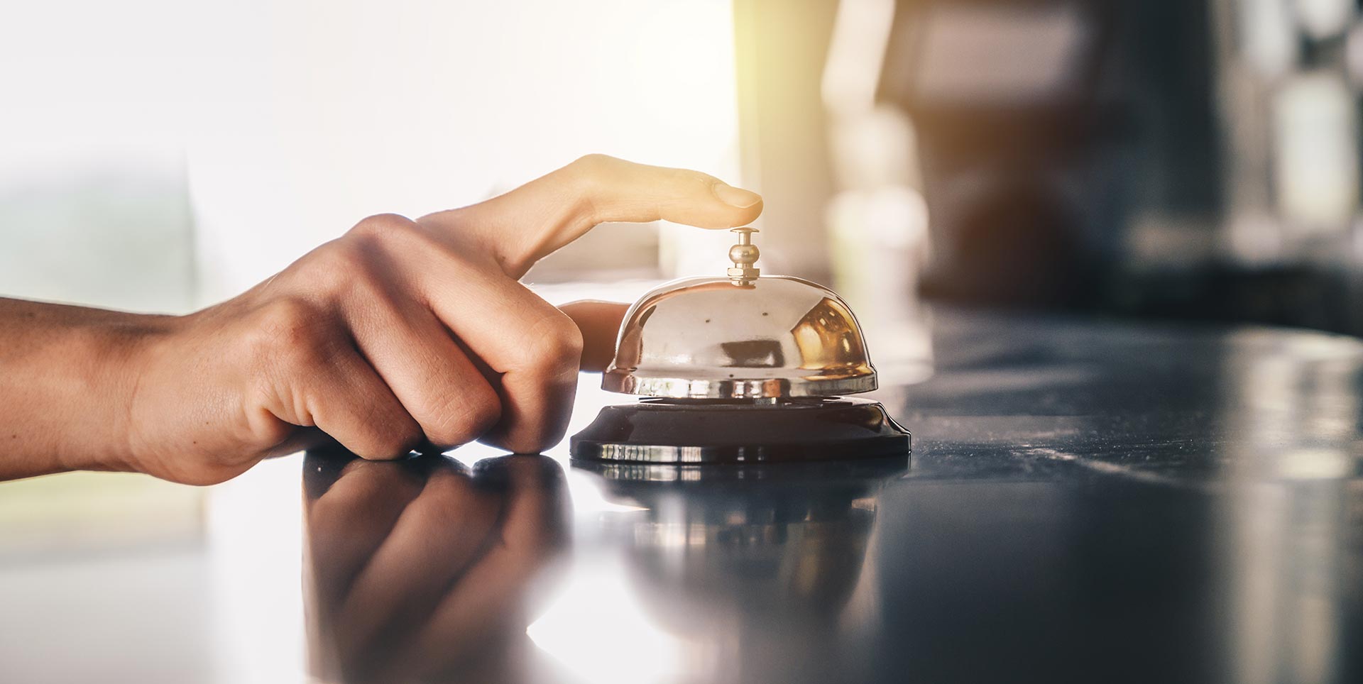 A person pressing a bell button with their finger on top of a countertop.